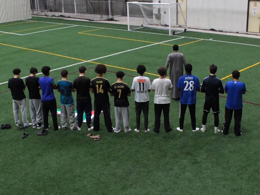 A row of players standing shoulder to shoulder in prayer on the turf