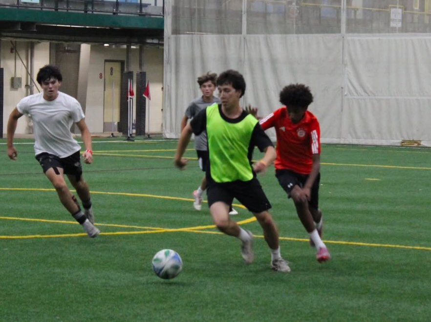 A player carrying the ball past two defenders on the indoor pitch