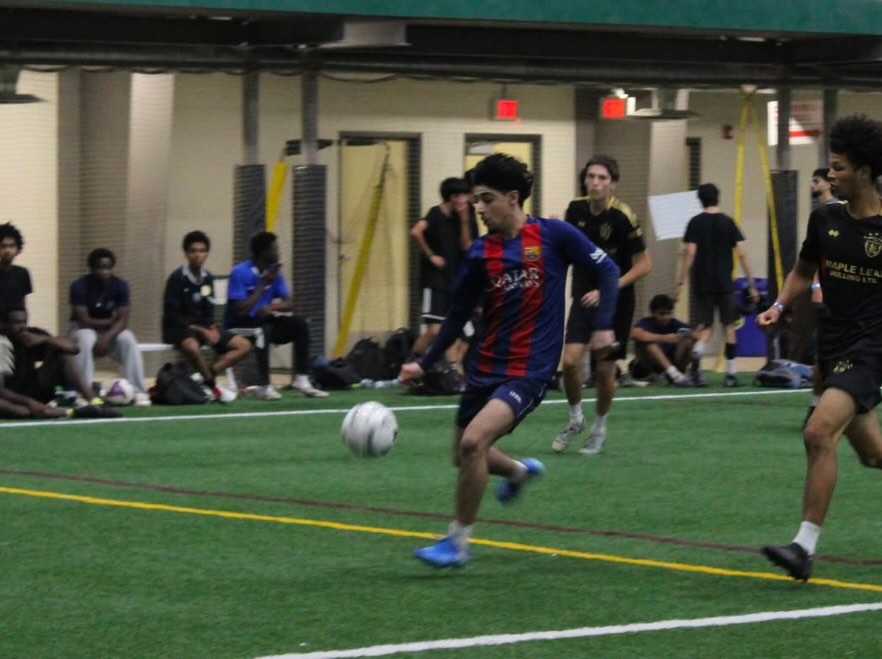 A player driving forward with the ball while the sideline watches